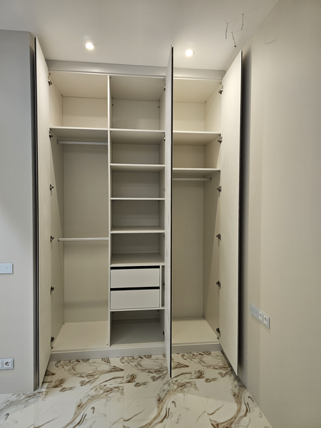 Внутреннее наполнение Внутреннее наполнение шкафа с продуманной системой хранения: секции для короткой и длинной одежды, центральный блок с полками и выдвижными ящиками, а также дополнительные полки в верхней зоне. Конструкция рассчитана на удобную сортировку вещей, эргономичное использование пространства и повседневный комфорт, с аккуратной фурнитурой и точной геометрией всех элементов.