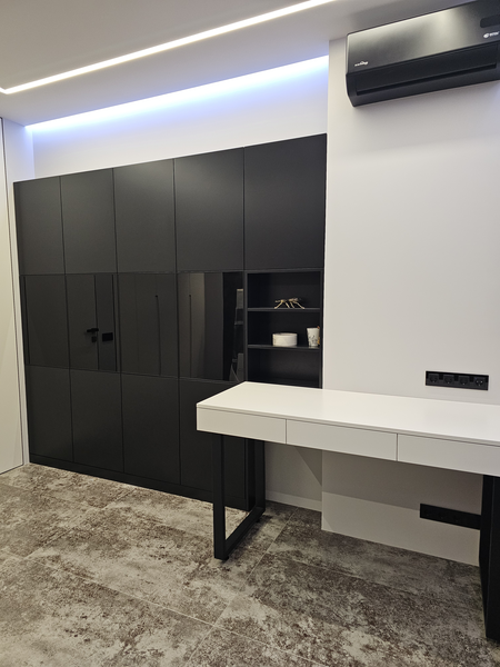 Многофункциональная встроенная Многофункциональная встроенная система хранения во всю стену: сочетание закрытых чёрных фасадов, зеркальных поверхностей и открытых полок, выполненная на заказ мебель формирует единое архитектурное решение с рабочей зоной и скрытым хранением.
