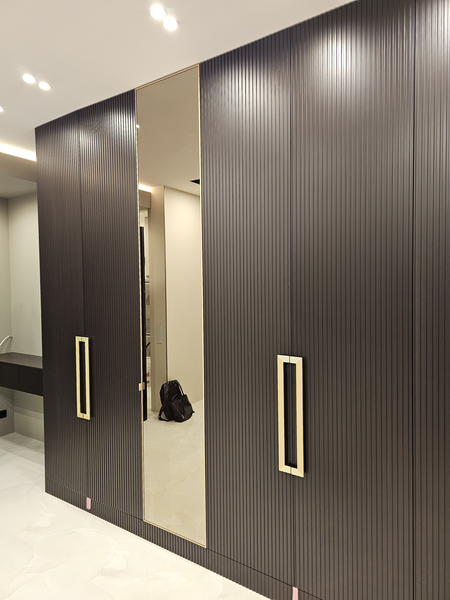 Общий вид Общий вид фасадов корпусной мебели с рифлёной текстурой, центральной зеркальной панелью и симметричным расположением дверей, создающих эффект монолитной стены хранения в современном интерьере