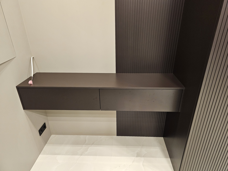 Подвесная консоль Подвесная консоль из корпусной мебели с двумя выдвижными ящиками без видимых опор, выполненная в тёмном матовом исполнении, интегрированная в систему хранения и визуально объединённая с фасадами шкафа
