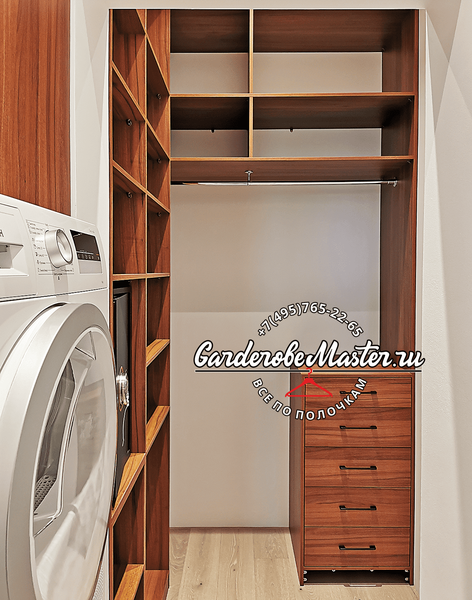 Гардеробная комната Гардеробная комната с корпусной системой хранения из натурального шпона, включающая вертикальные открытые полки, секции для длинной и короткой одежды на металлических штангах и мобильный блок ящиков, интегрированная в узкое помещение с бытовой техникой