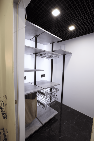 Фрагмент открытой гардеробной системы с серыми полками, металлическими опорами и выдвижным блоком ящиков, демонстрирующий архитектурную геометрию, глубину хранения и аккуратную интеграцию освещения.