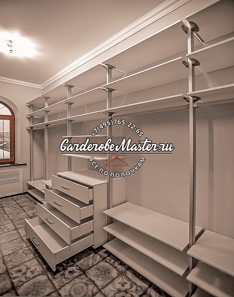 Открытая гардеробная система с металлическими стойками и полками, выстроенная вдоль стены, с модульными секциями для хранения одежды, обуви и аксессуаров, выполненная в светлом оттенке с равномерной архитектурной композицией