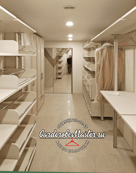 Просторная гардеробная комната с симметричными секциями хранения, выдвижными обувными полками, штангами для одежды и центральным зеркалом, выполненная в светлой нейтральной палитре