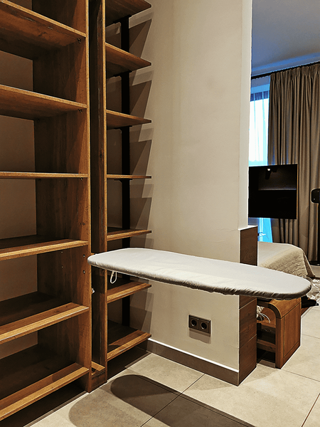 Открытая гардеробная система в мансардном пространстве с интегрированной гладильной доской, вертикальными стойками и полками из натурального дерева, выполненная по индивидуальному проекту