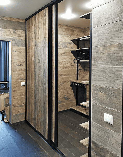Раздвижные двери для гардеробной с фасадами под натуральное дерево и чёрным алюминиевым профилем, скрывающие внутреннюю систему хранения