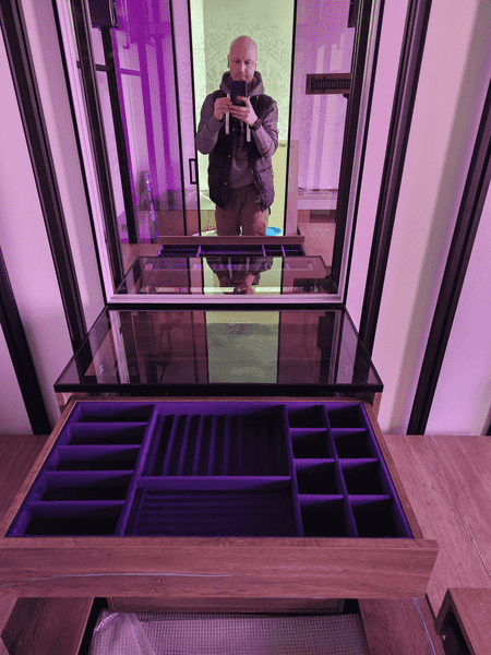 Зеркальная зона Зеркальная зона гардеробной с центральным комодом и стеклянной поверхностью, комбинирование дерева и металла, мягкая цветная подсветка интерьера